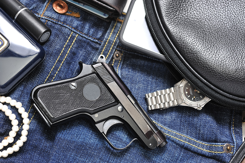 The purse of a women with items like gun, watch and lipstick on display