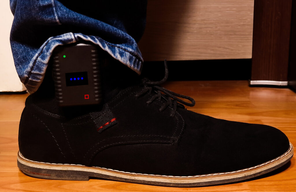close up view of an ankle monitor worn under jeans